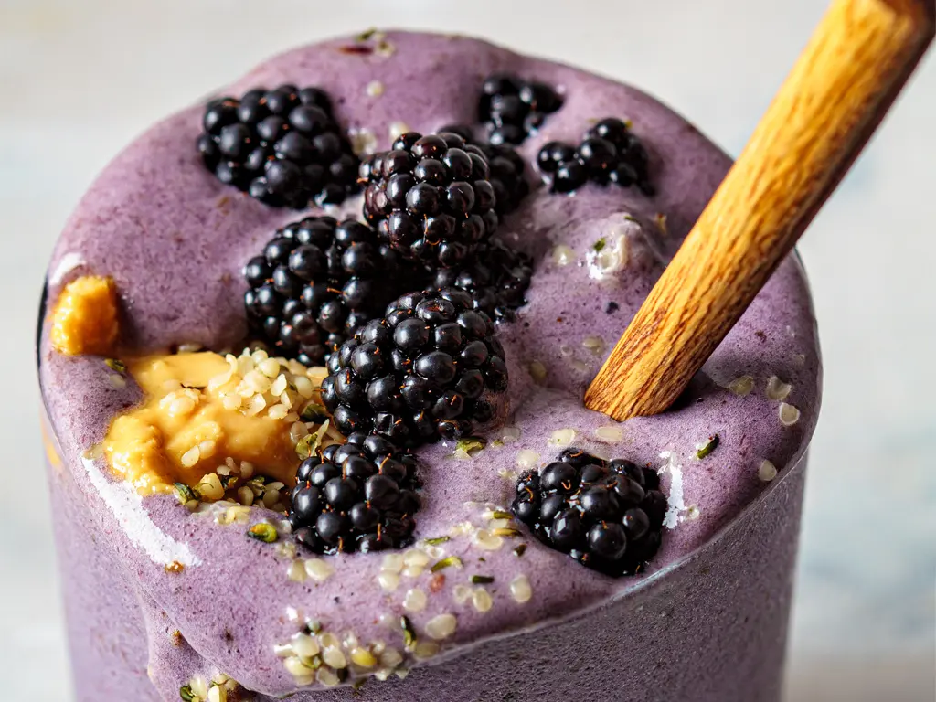 A plant based smoothie topped with peanut butter, hemp seeds, and fresh black berries.